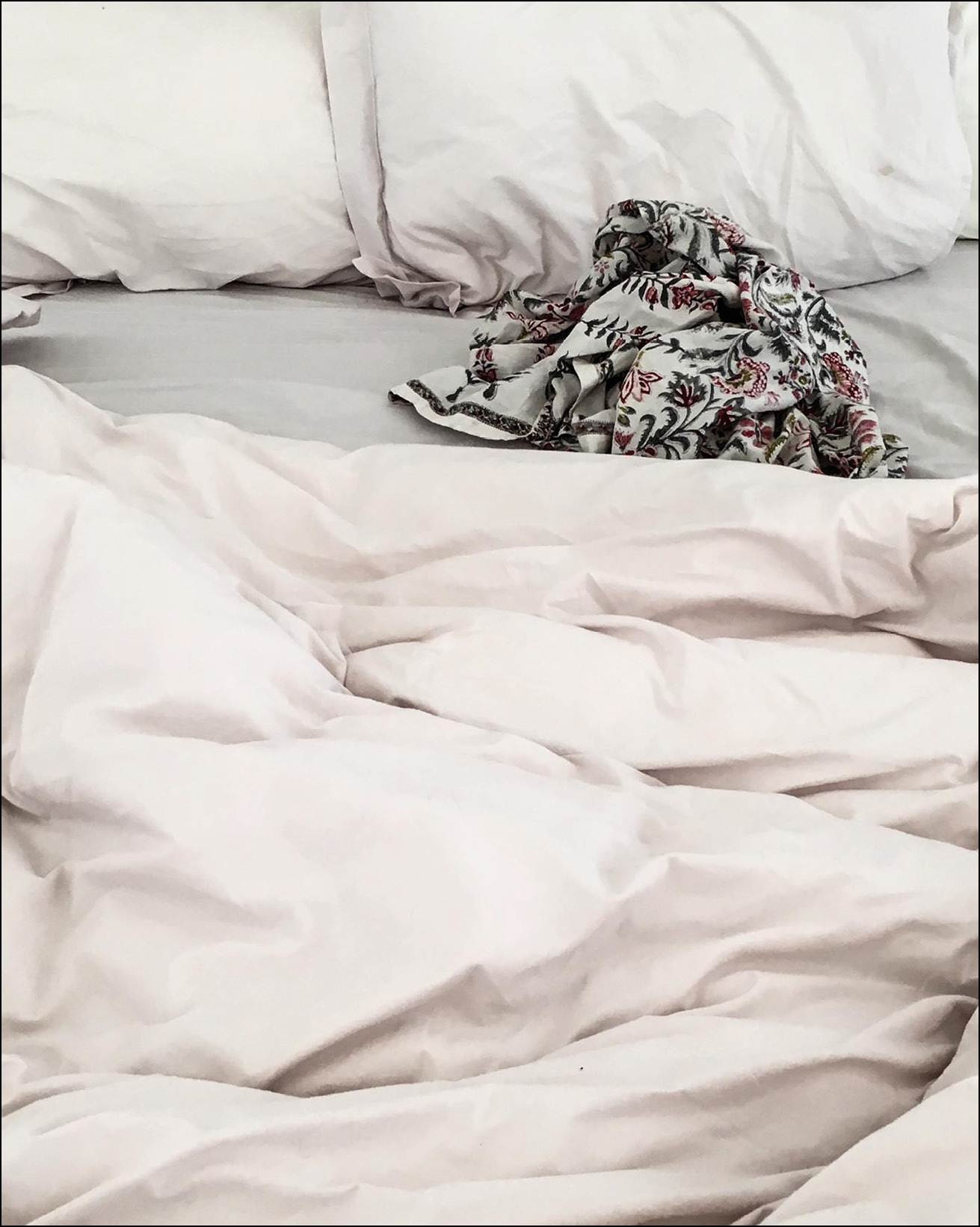 A bed with pillows and sheets that have been slept and tossed around in, and a crumpled patterned cotton nightdress