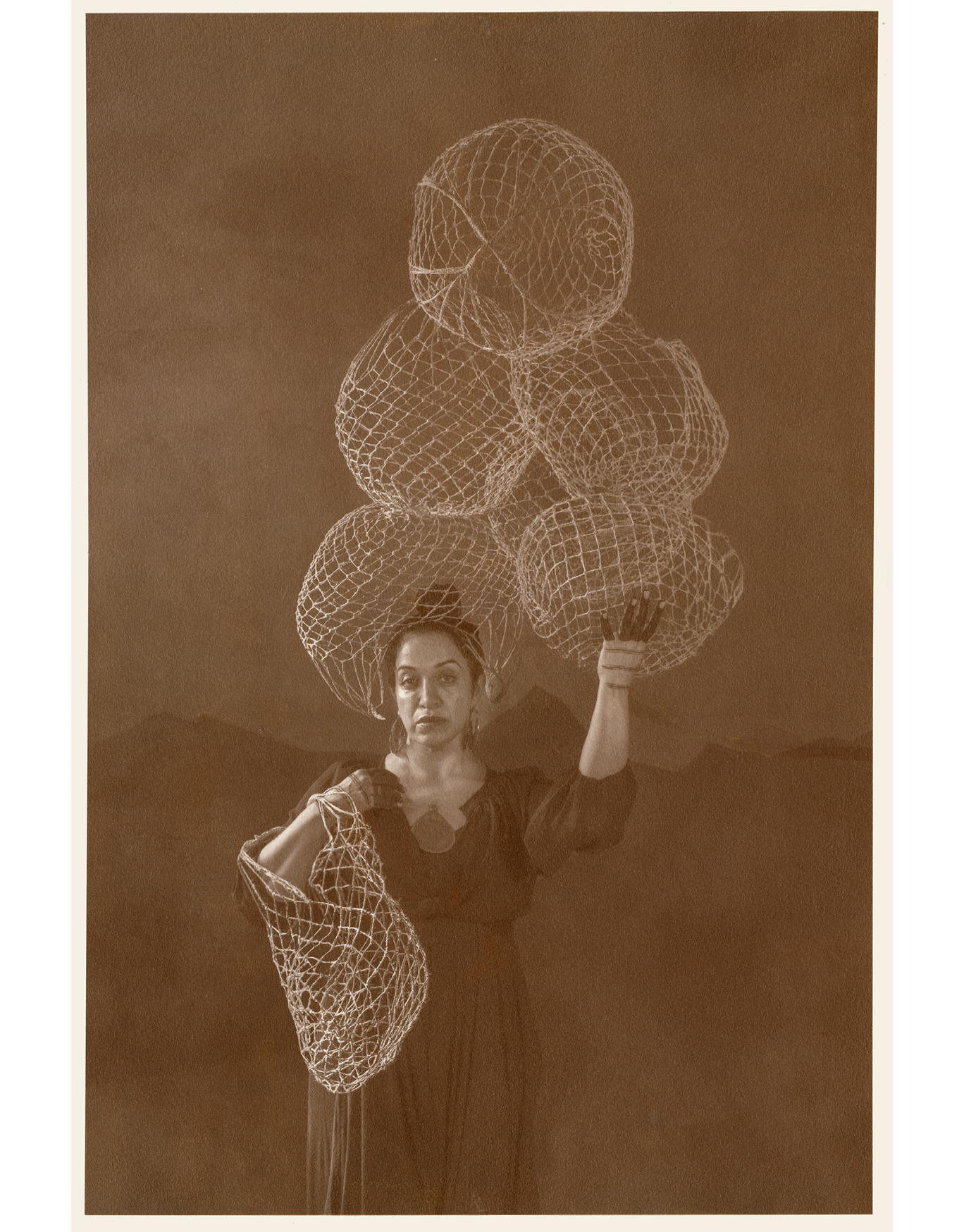 Brown toned photographic portrait of a woman, holding a stack of woven jute baskets over head, and carried on one arm. It appears the circular baskets are filled with an empty space. Her hands have henna black stripes printed on them.