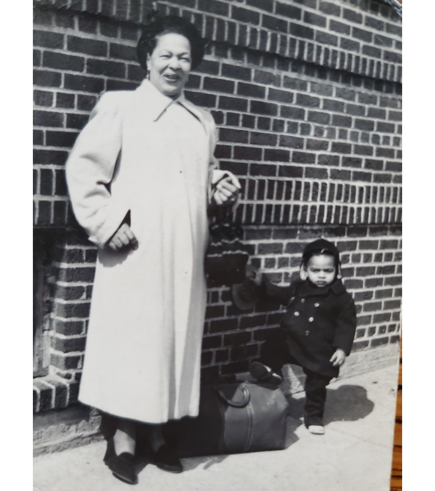 Fig 2. Black and white image of a woman in a long coat with a child posing in front of a brick wall.