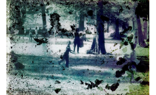 A small group of children play in a wooded park among tall trees. A woman holds a bag and watches them play. The image has been obscured by damage, with black dots and smudges, and the color turned various tones of green. 