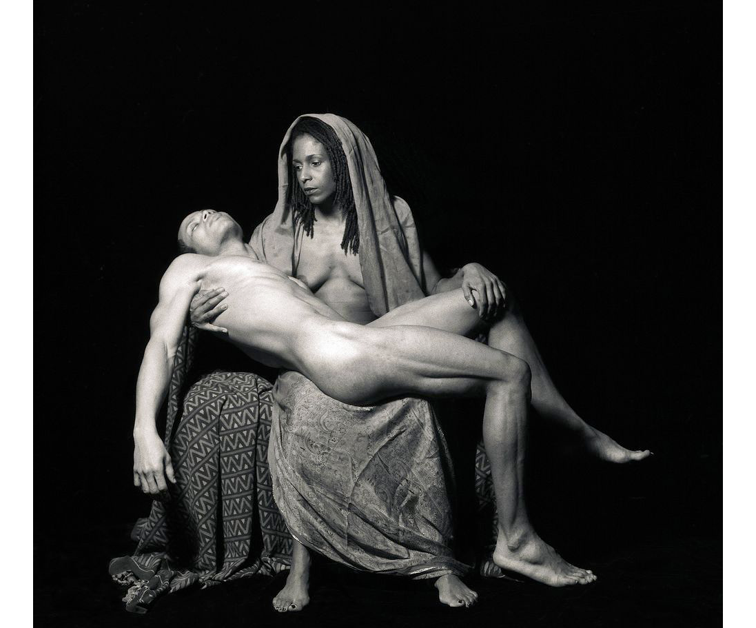 Black and white image of a woman in robes holding a naked man in her lap. 