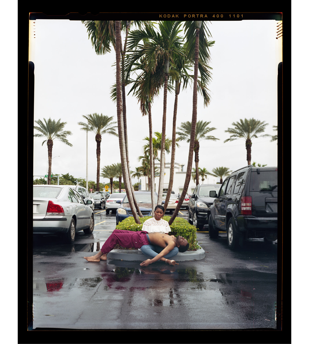 Images of a young boy who is sitting in the road, sounded by cars, and palm trees. There is a man laying across the boy's lap