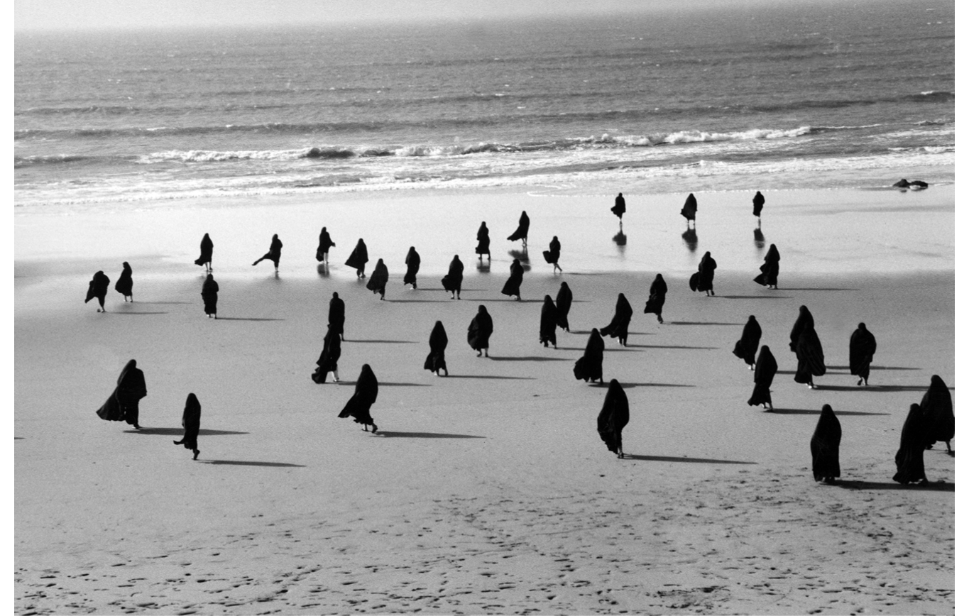 This image from Shirin Neshat?s double-channel video installation Rapture, captures a fleeting moment towards the end of the narrative in which a group of black-veiled women are seen from the back walking towards a vast, open seascape. Their veils are billowing in the wind, creating silhouettes that are reminiscent of birds, which placed within this natural landscape constitute a female space that starkly contrasts the masculine realm created by Neshat in the opposite channel not shown here.