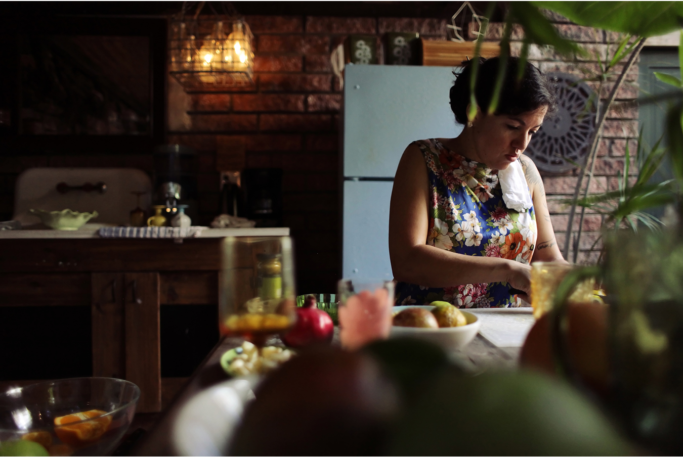 Image of a woman at a kitchen counter. The counter has plants, fruits and bowls spread across it. 