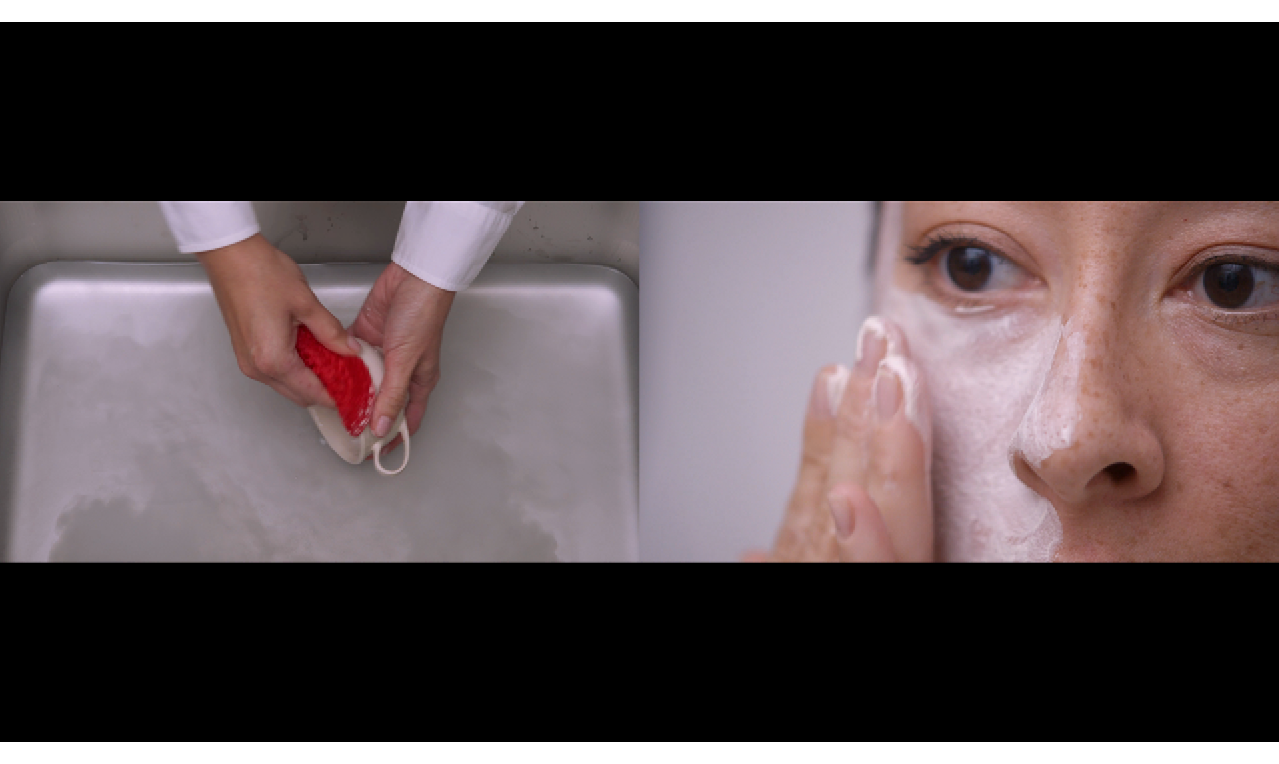 Video still with two images. The left side shows two hands with whtite shift cuffs washing a cup with a red sponge. THe right side shows a woman spreading white cream on her face with her fingers.