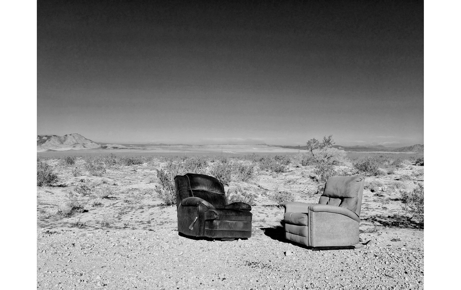Two abandoned chairs, one black, one white, in a desert landscape.