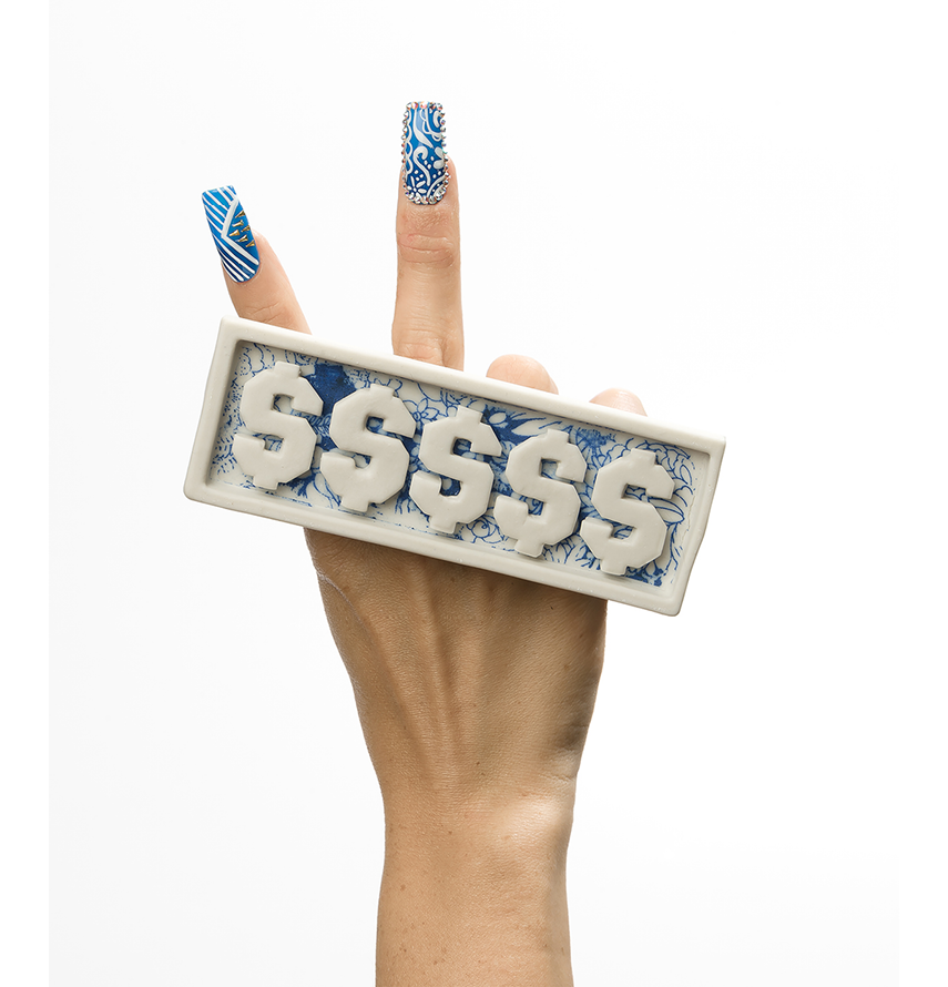 Image of a hand making the peace sign (hand gesture in which the index and middle fingers are raised and parted to make a V shape while the other fingers are clenched.) The index finger and middle finger have long acrylic nails with white and blue patterns. There is a porcelain plate ring with money signs going across