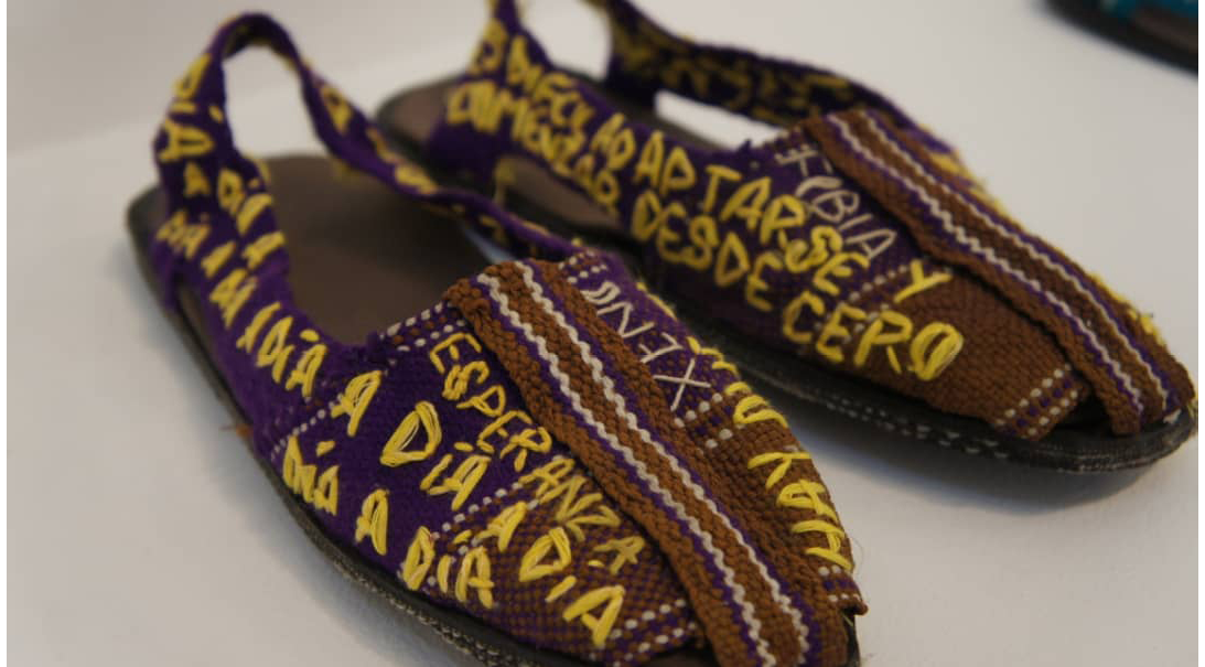 Two purple espadrilles. Some phrases are embroided with yellow thread. They are written in Spanish: ""day by day""from scratch"".