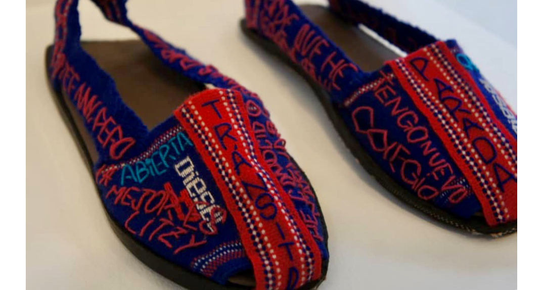 Two espadrilles woven in red and purple threads. Some phrases are embroided with threads of different colors. They are written in Spanish: ""I have new school""stop""Diesel""open"".