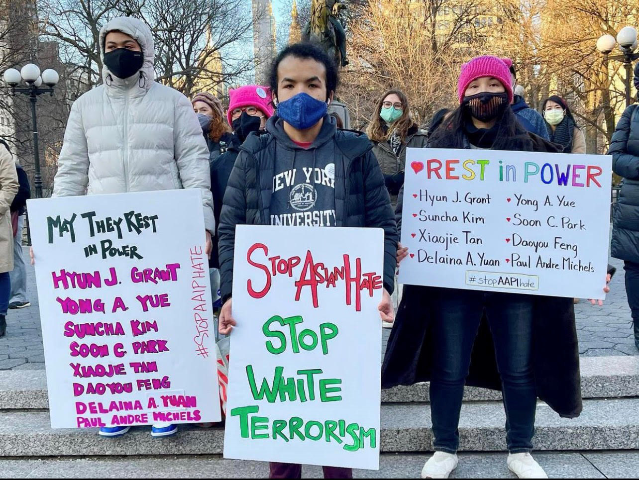 A photograph of protesters wearing masks. They hold placards with the names of dead, and slogans such as ""Stop Asian Hate"" and ""Stop White Terrorism