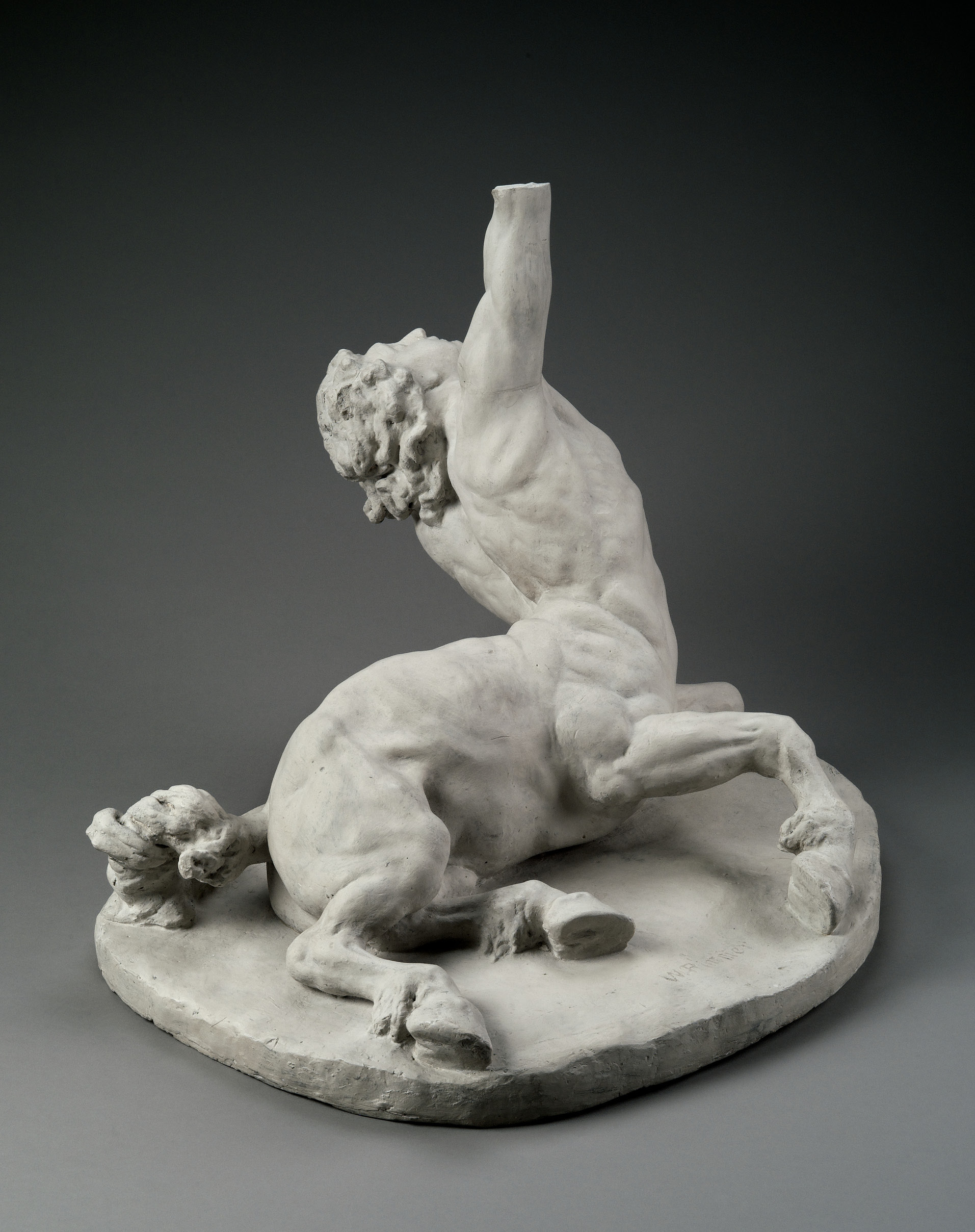 A plaster sculpture of a centaur, its lower animal half lying on the ground while its human half is lifted up, his arm reaching up above him and his head turned upwards.