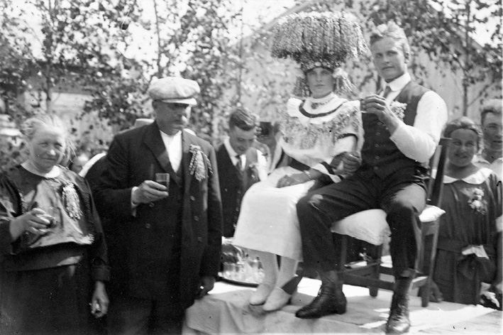A newlywed couple in Vörå in Ostrobothnia seated on a table and receiving congratulations (1925). Photograph by Erik Hägglund.
