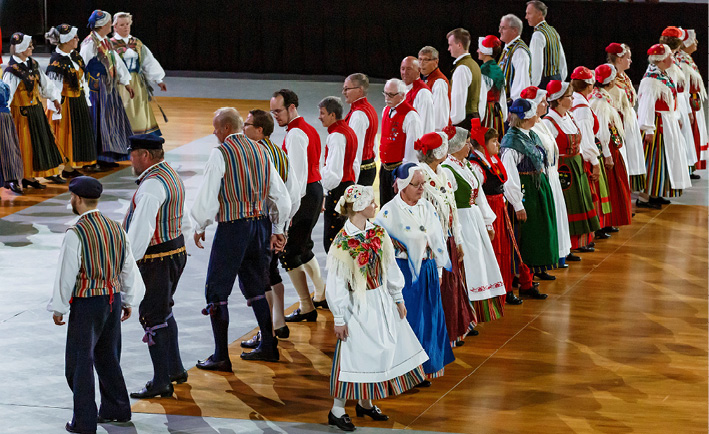 A large group of Finnish Swedish folk dancers in traditional costumes perform a minuet from Oravais in Turku (2017). Partners have passed each other are about to turn around to face each other again, photograph by Timo Hukkanen.