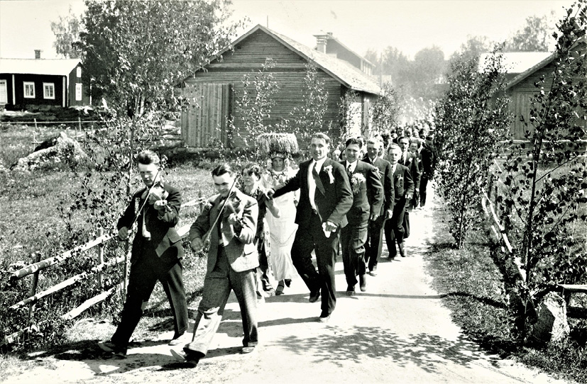 Wedding entourage in Vörå (1934). Two fiddlers leading, followed by the bridal couple and guests, photograph by Erik Hägglund.