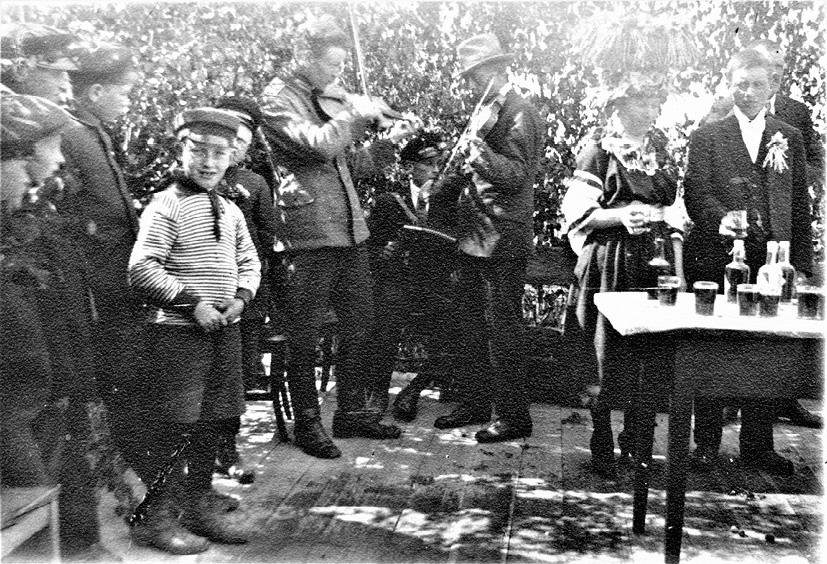 Wedding in Vörå (1922). The bride and groom toast with the guests while two fiddlers and an accordionist are playing, photograph by Erik Hägglund.