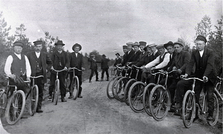 Men are lined up along a road with their bicycles in Ostrobothnia (1922). In the background, it appears that there is a fight going on, photograph by Erik Hägglund.