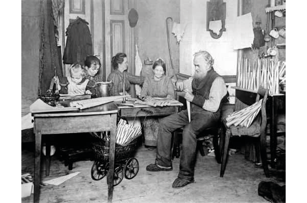 A black and white photograph of several generations of a German family ca. 1900; shows five members of a family working on various tasks in a single room.