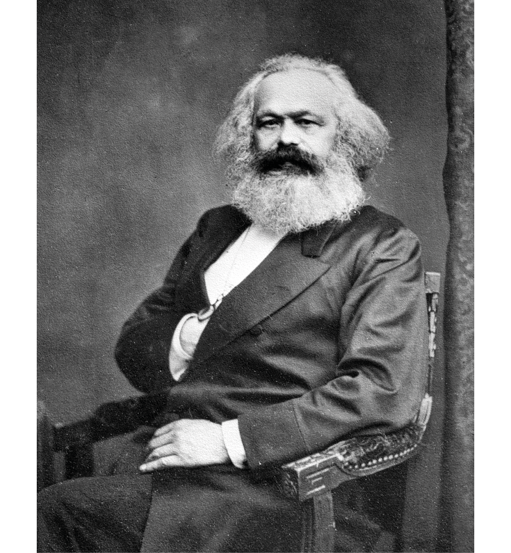 A black and white portrait of german philosopher Karl Marx; shows Marx sitting in a wooden chair, posing with his right arm in his vest pocket and his left hand over his left thigh.