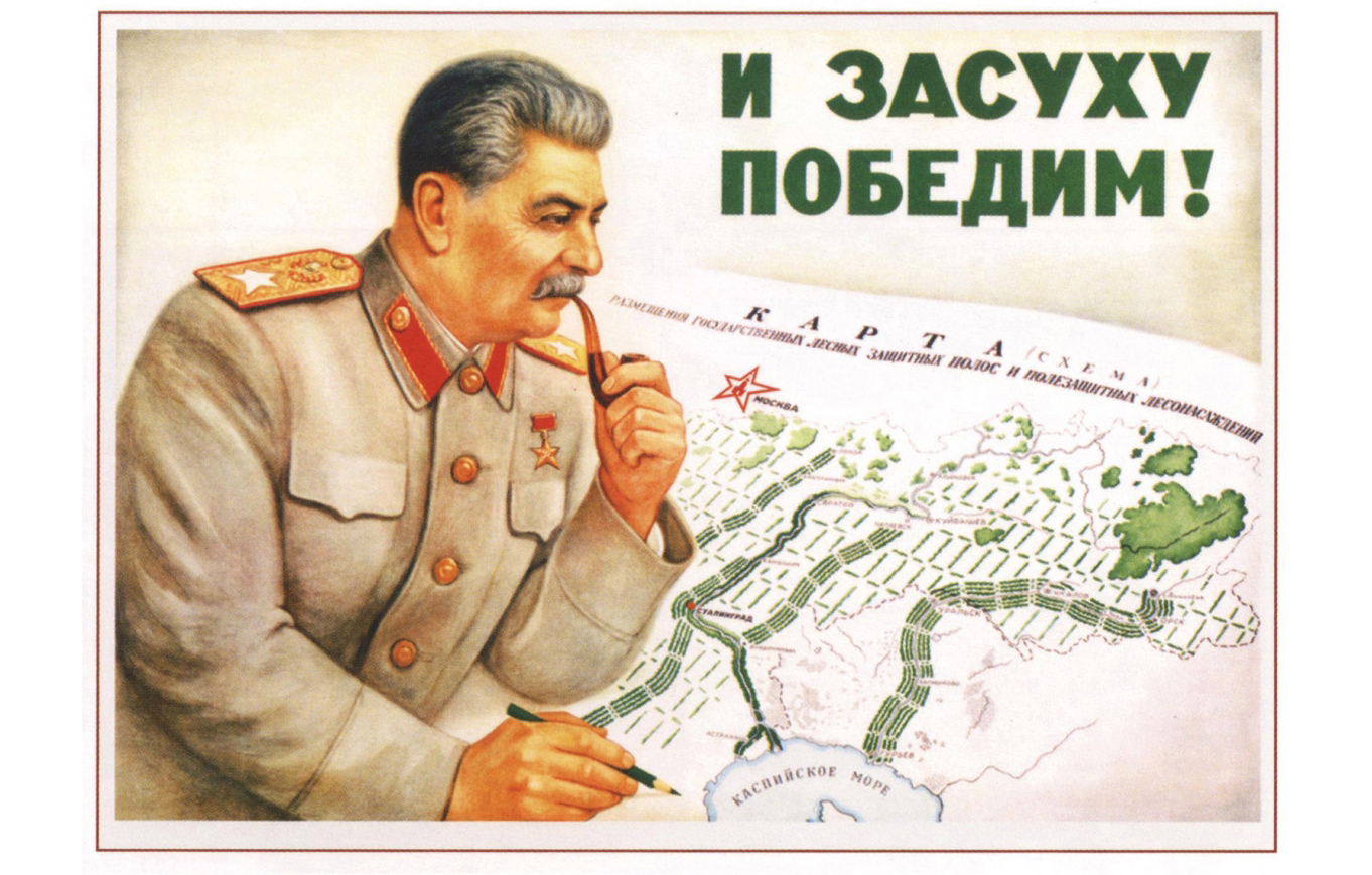 Propaganda image from 1949: shows Stalin in Soviet military uniform leaning over a Russian map holding a pipe to his mouth with his left hand while holding a green pencil with his right; on the top right-hand side a green lettered text reads a slogan in Russian 'Ð¸ Ð·Ð°Ñ�ÑƒÑ…Ñƒ Ð¿Ð¾Ð±ÐµÐ´Ð¸Ð¼' or 'We'll conquer drought, too'.