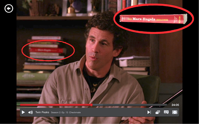 A screenshot from the show "Twin Peaks" - a man sits in the middle of the screen, mid-conversation, behind him is an out-of-focus bookshelf, one book is circled and a clearer shot of it is shown in the top right-hand corner, the title is "The Marx-Engels Reader".