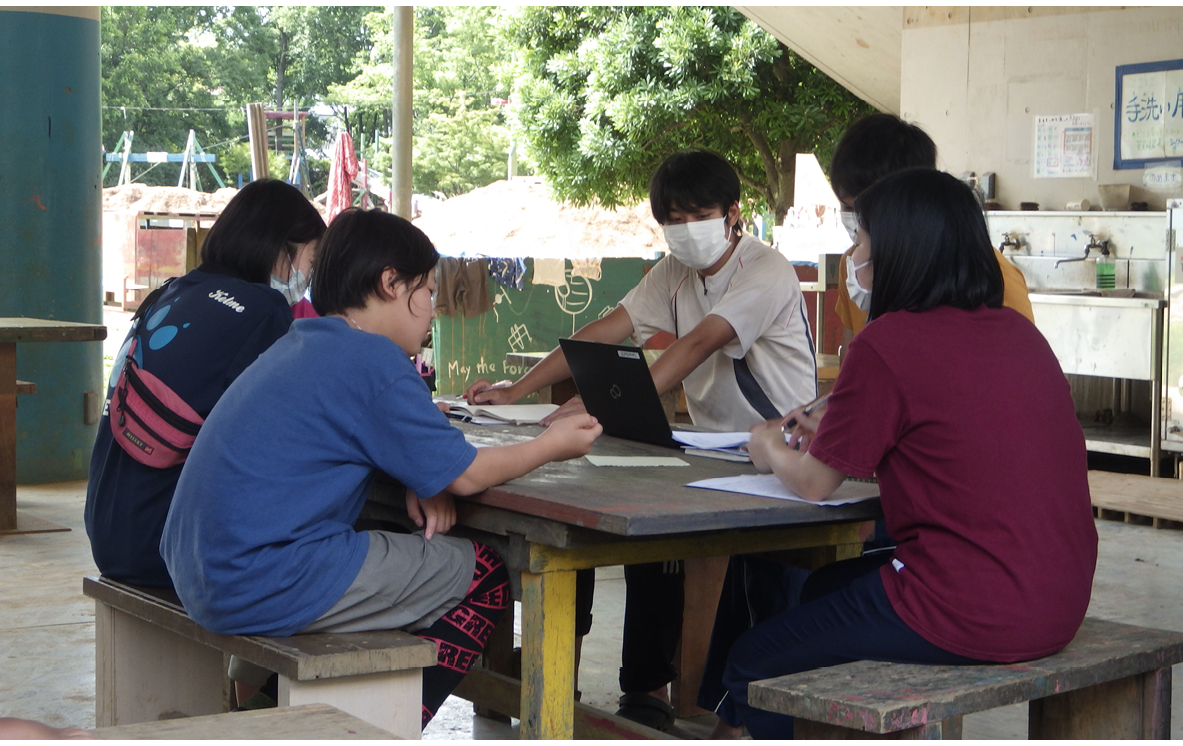 Playworkers sitting around table in adventure playground with laptop and papers