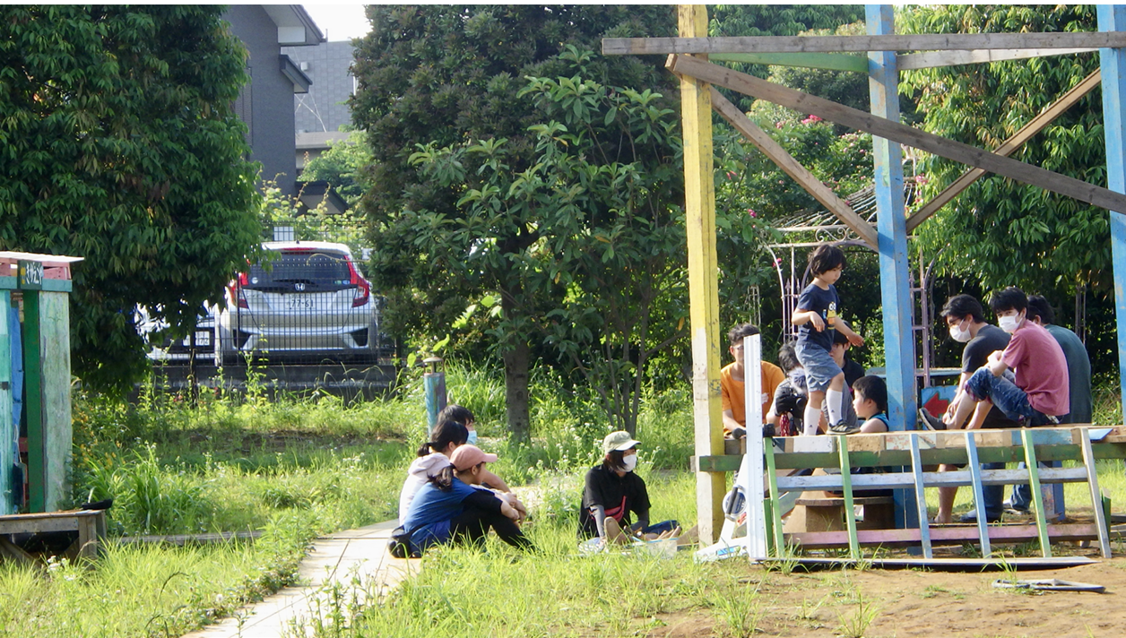 Children and playworkers sitting outside on grass and on wooden platform discussing