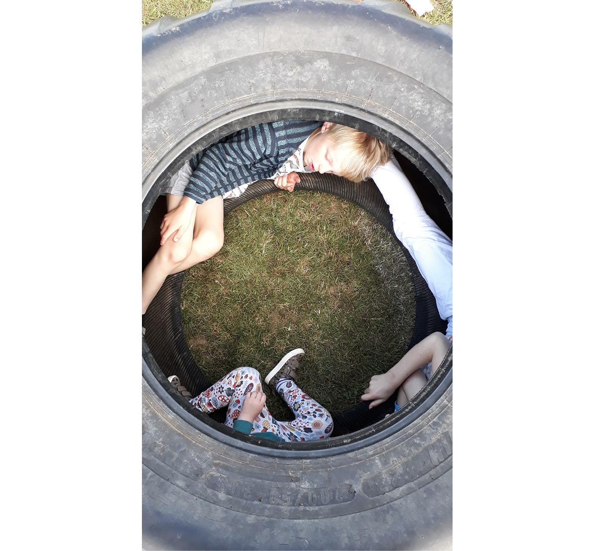 Photo looking down on three children nestled in inside rim of a tractor tyre