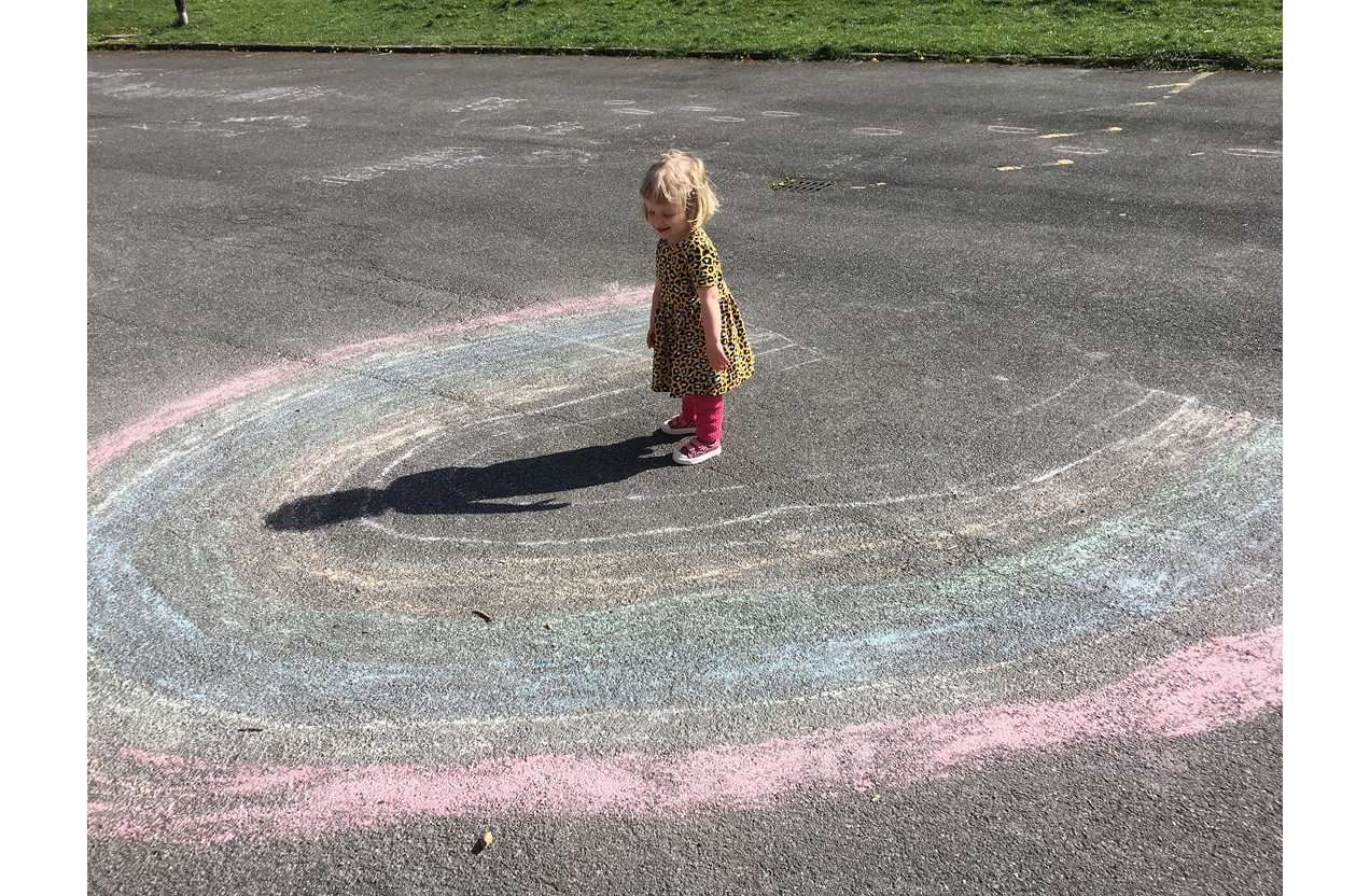 Photo of a small child standing in centre of rainbow chalked onto the ground