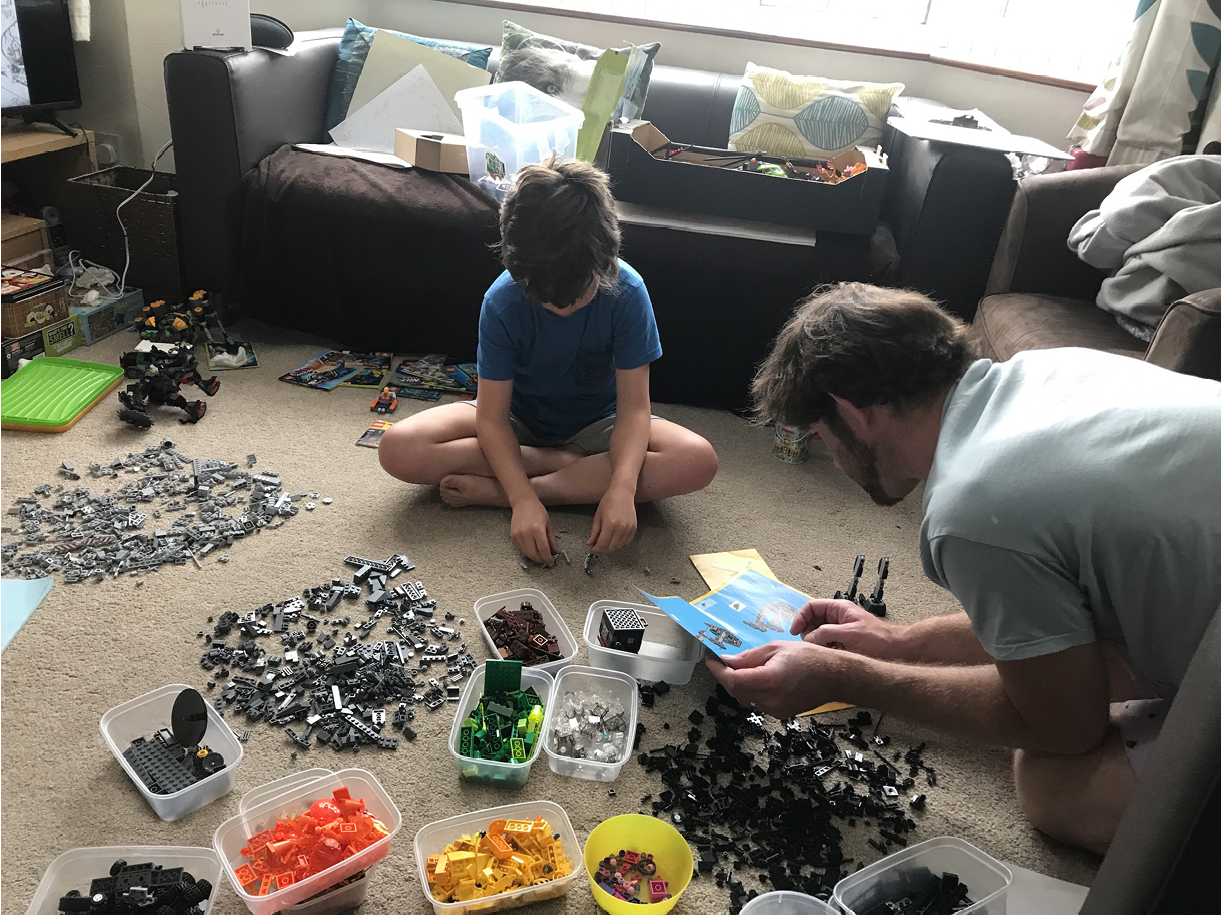 Photo of child and adult sitting on the floor with tubs of LEGO pieces, adult is reading instructions