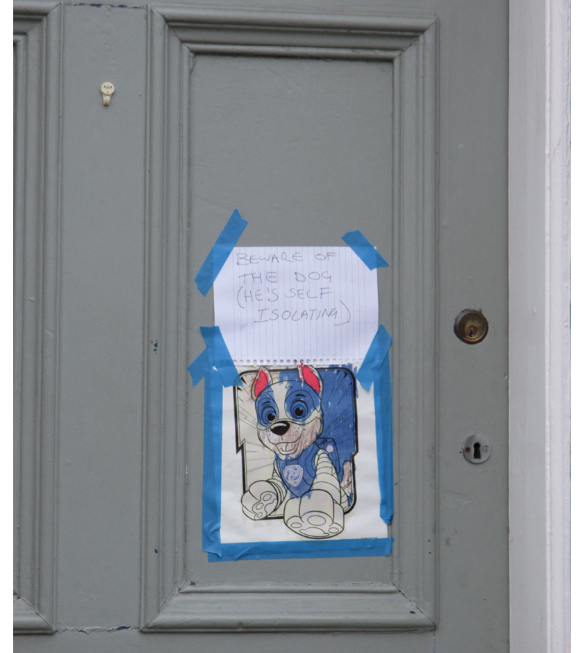Photo of a grey-painted front door taped to which is a note saying 'Beware of the dog, he's self-isolating', with a partially coloured in print-off of a cartoon dog beneath