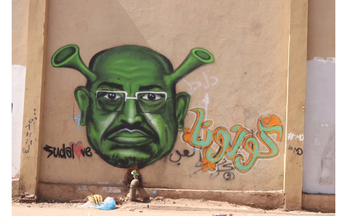 Painted in spray paint on a wall, a depiction of deposed head of state Omar al-Bashir with a green face and two horns emerging from his head, transforming him into a spikey Coronavirus