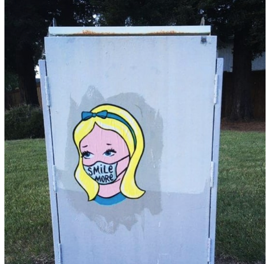 An image of a blonde child with a blue headband, easily identified as Alice in Wonderland. She wears a face mask with text reading 'smile more' written on it.