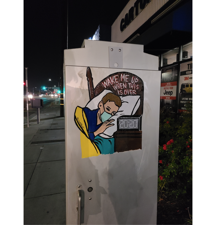 This wheat paste shows a child tucked in and sleeping peacefully. He is covered by a bright yellow blanket and he wears blue plaid pajamas and a turquoise medical mask. The time on the alarm clock reads 2020 and text on the headboard reads 'Wake Me Up When It's Over.'