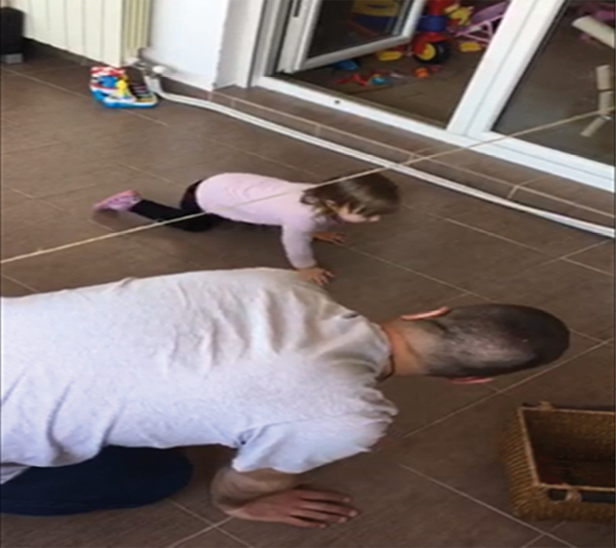 Photograph of father and child crawling on floor under horizontally suspended string