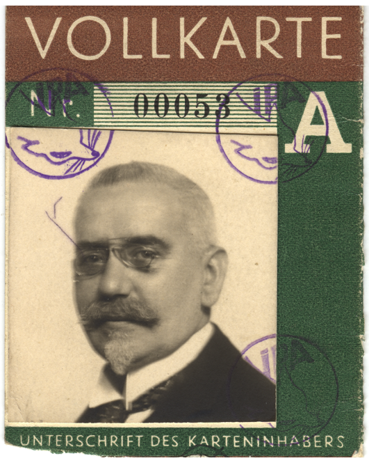 A sepia-toned photograph of a bespectaled man with a light beard and moustache on a dark green entry pass to the International Fur Trade Exhibition with blue stamps