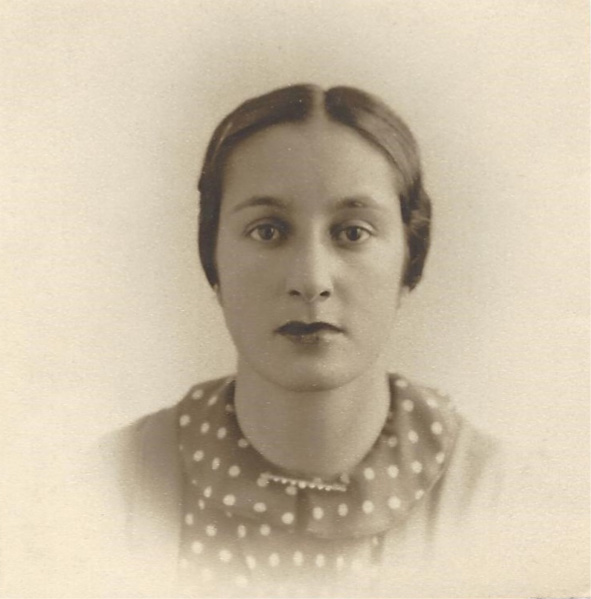 A sepia-toned portrait of a dark-haired woman in her twenties looking directly into the camera wearing a polka-dot shirt and dark lipstick
