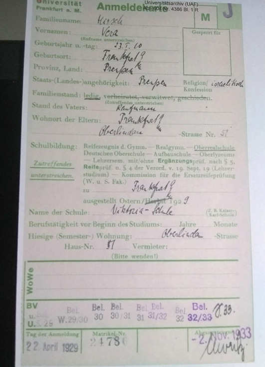 A colour photograph of a cream Nazi registration card with blue ink writing and green printed writing