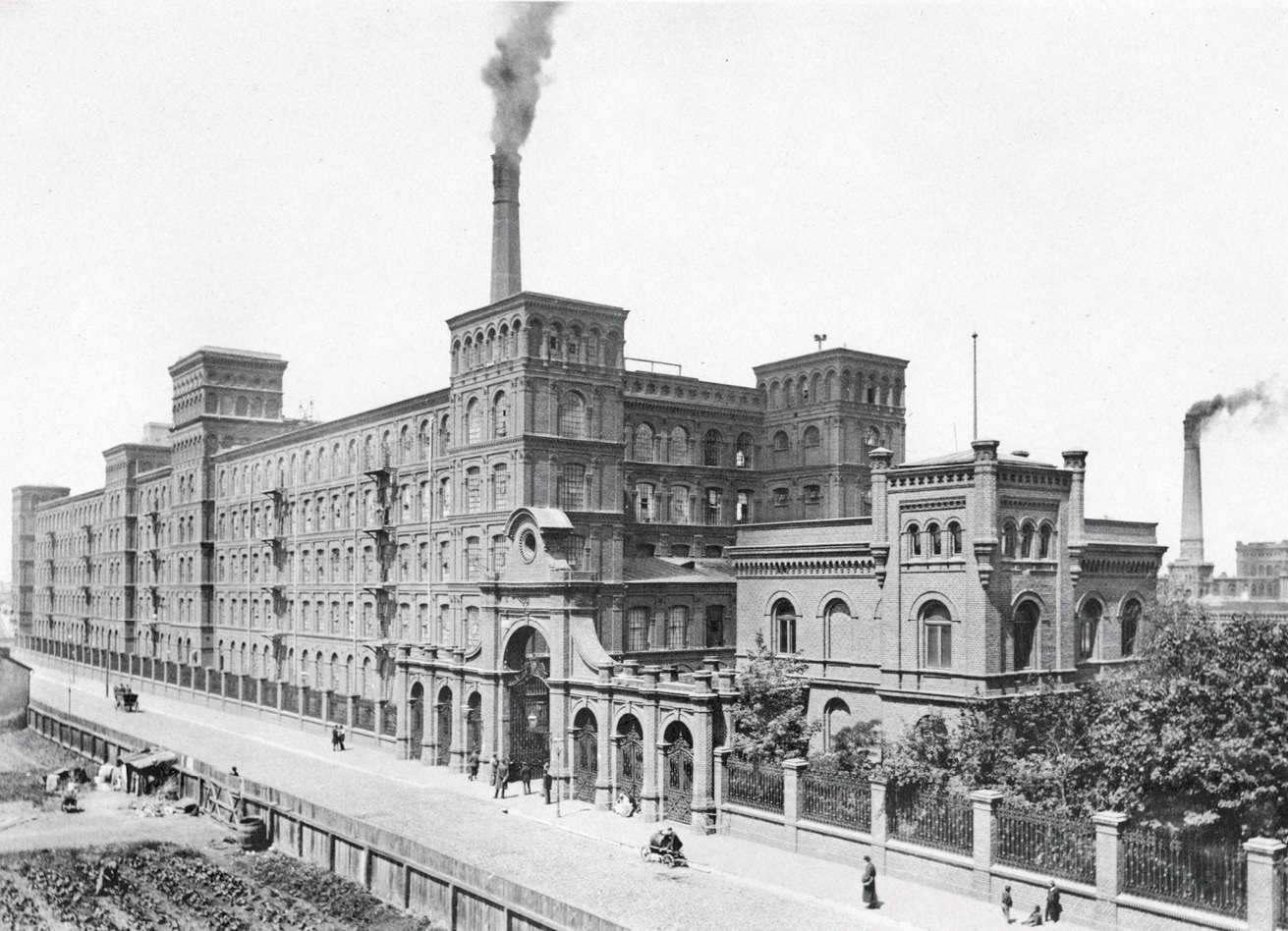 People strolling or sitting on the sidewalk along the facade of the Poznanski textile factory in Lodz, Poland.