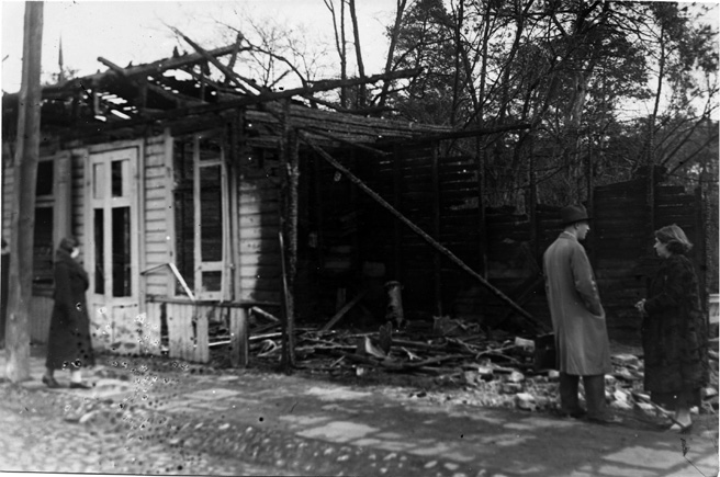 The photo shows three people examining the burnt remains of a house that was burned down in the June 1936 Minsk-Mazovyetsk pogrom.