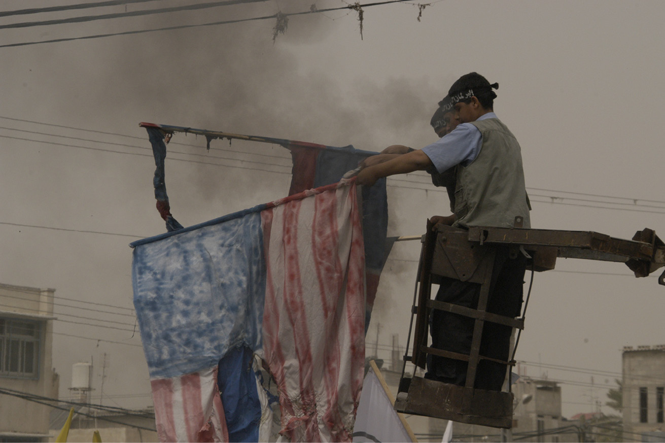 Three men standing in an elevated passenger basket and burning flags.