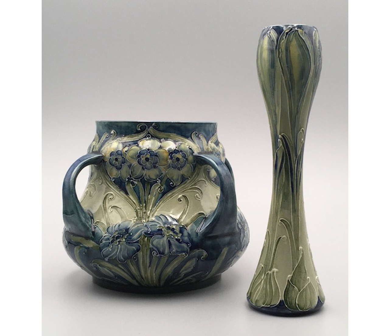 A four-handled squat vase decorated with Narcissi; a slender vase decorated with a crocus rising from its corm. Both are painted in a blue, green and yellow colourway associated with pots made for Liberty & Co.",,,