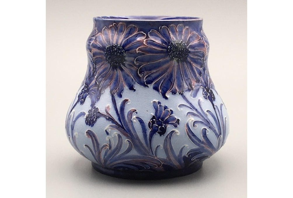 A vase of squat, undulating form, decorated with daisies in dark blue with pink and yellow highlights against a pale blue ground.",,,