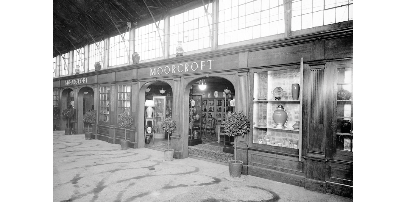 A long frontage with four arched entrances beneath the name Moorcroft; above, four large vases are displayed.   Cabinets contain a range of pieces from tea wares to decorative vases; clipped trees in pots flank the entrances.    ",,,