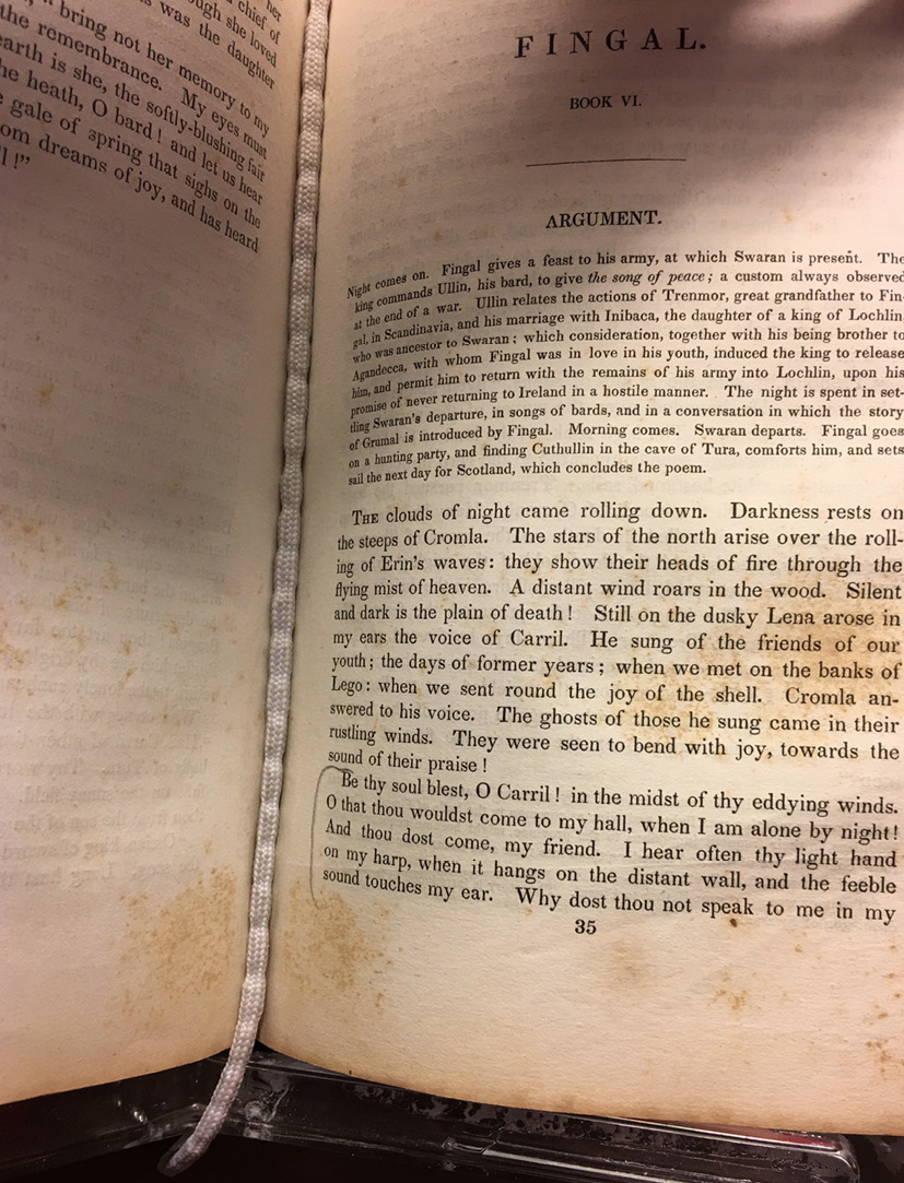 An old printed book with mottled pages held open on page 35, with a book snake running down the middle of the book to keep the pages open safely.