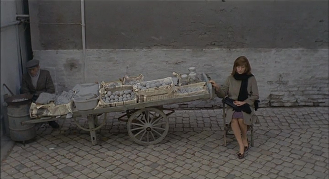 A scene from ‘Il Deserto Rosso’ (Red Desert) (1964) by Michelangelo Antonioni. A solitary woman sits next to a cart filled with objects, the muted colors evoking the film’s themes of alienation and modern industrial landscapes.”,