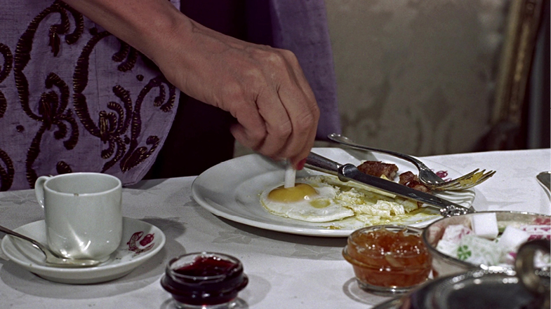 A close-up of a character in ‘To Catch a Thief’ (1955), delicately salting a fried egg with a cigarette, another odd yet sophisticated action typical of Hitchcock’s use of visual humor amidst suspense.”,