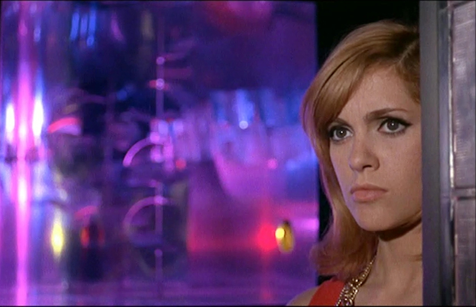 A scene from the 1968 French psychological drama “”La Prisonnière”” directed by Henri-Georges Clouzot. The image captures a close-up of a woman with auburn hair in an intense gaze, set against a vivid and colorful background with purple, pink, and blue lighting.”,