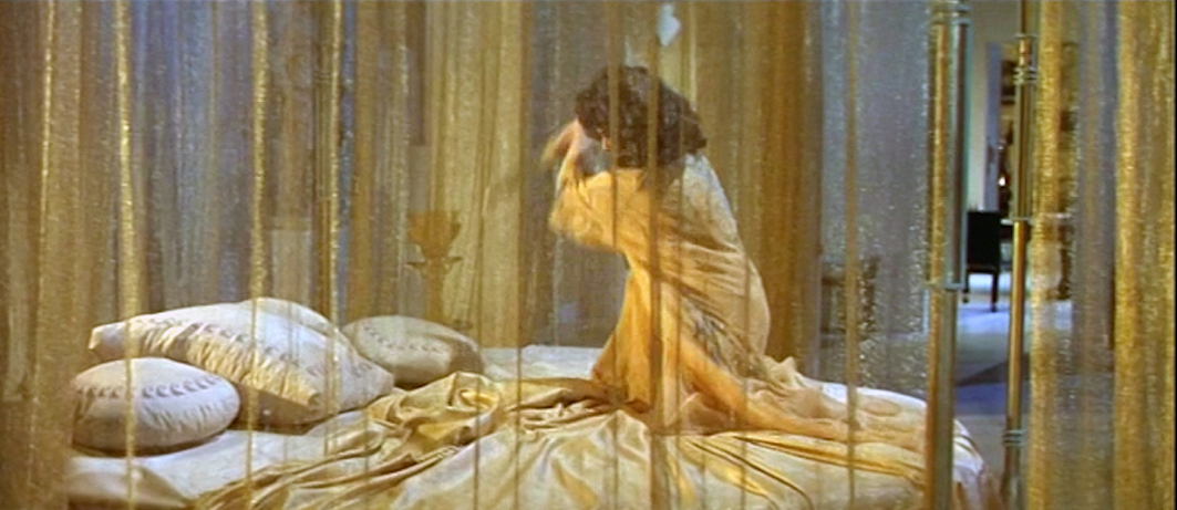 A still from the 1963 epic historical drama film ‘Cleopatra’, directed by Joseph L. Mankiewicz. The image shows a woman, presumably Cleopatra, waking up in a luxurious bed draped in golden curtains. The scene conveys the opulence and grandeur associated with Cleopatra’s rule in ancient Egypt.”,
