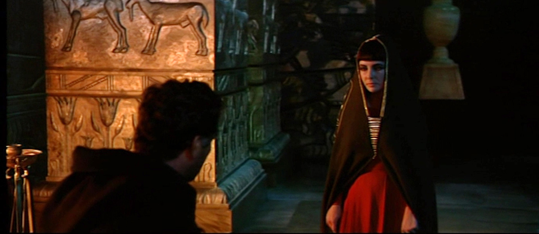 A scene from the 1963 historical epic ‘Cleopatra’. The image captures a solemn moment where Cleopatra, dressed in a black cloak, stands in a dimly lit chamber. Hieroglyphics and ancient Egyptian motifs can be seen on the wall behind her, reinforcing the film’s historical setting.”,
