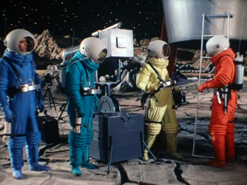 A scene from ‘Destination Moon’ (1950) with four astronauts in colorful space suits standing on a rocky moon surface near their spaceship. The suits are blue, teal, yellow, and orange, with large, rounded helmets.”,